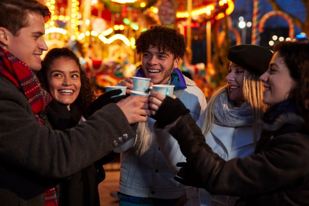 Group of friends at a Christmas market enjoying a warm festive drink and having fun