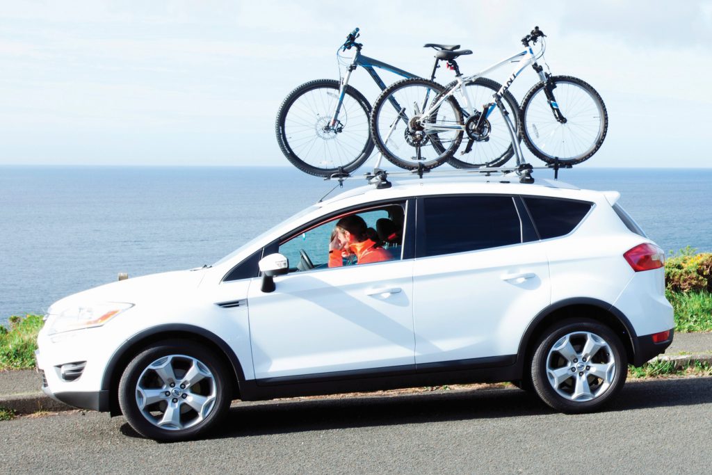 White car with pushbike rack on the road next to the coastline