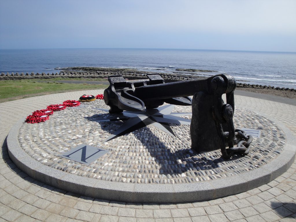 The anchor of Mona's Queen at Kallow Point in Port St Mary﻿ on a sunny day with red wreaths lay on the ground 