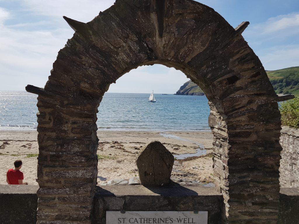The view through St Catherine's Well, a stone arch, onto Port Erin Beach and looking out to sea with a small yacht in the background