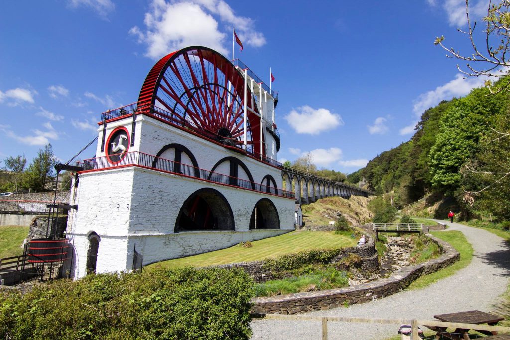 The Great Laxey Wheel on a sunny day showing a blue sky and pleasant  surrounding greenery 