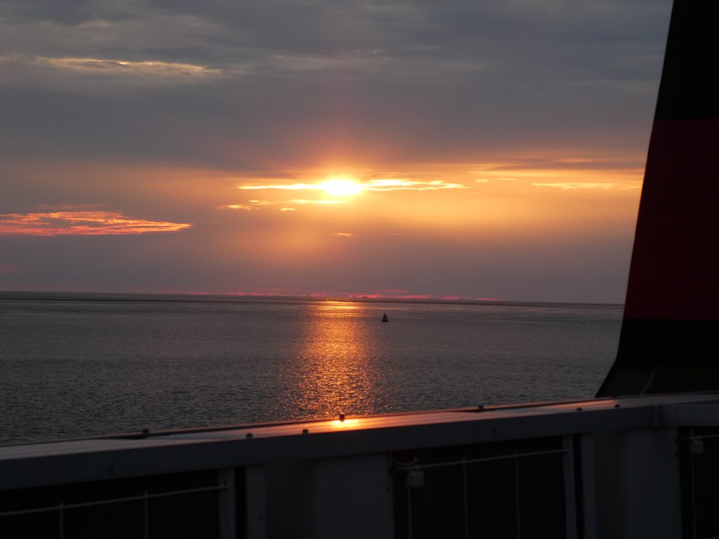 The sunset from the deck of fast craft Manannan showing an orange sun through the clouds 