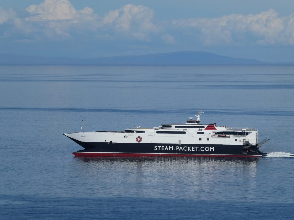 Steam Packet Company vessel Manannan arriving in Douglas Bay on a calm, blue sea with clouds and English hills in the far distance 