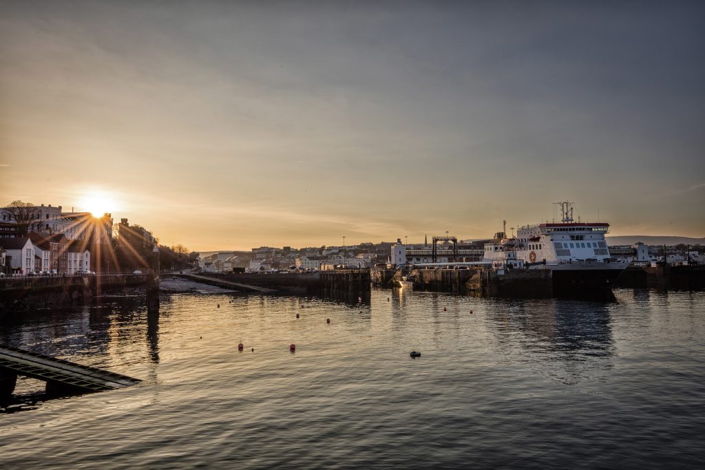 Image of Douglas Harbour with the sun setting in the background and the Steam Packet Company vessel Ben-my-Chree sitting in the harbour to the right of the image. 