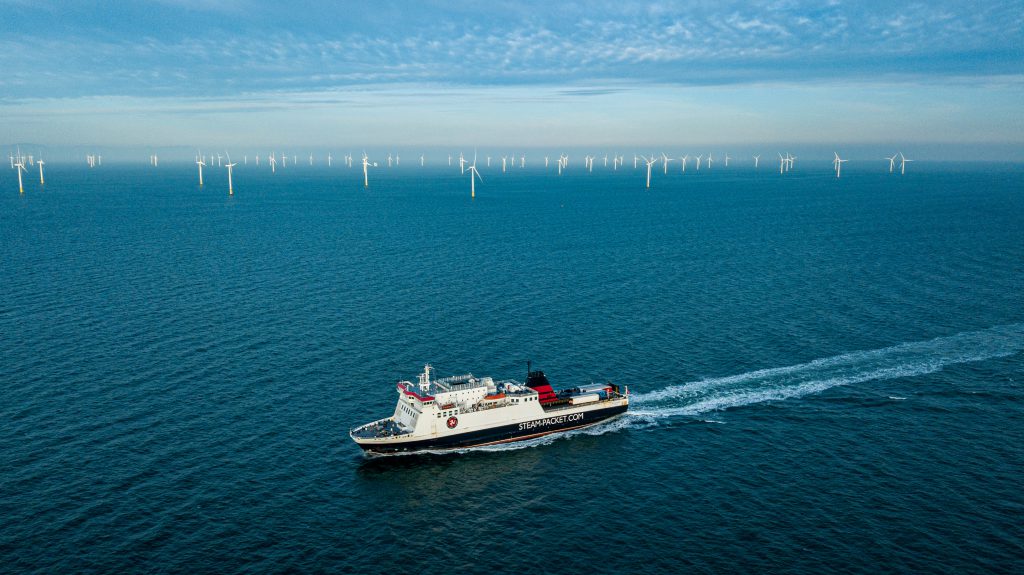 The Ben-my-Chree sailing in the Irish Sea with blue skies in the background and a wind farm 