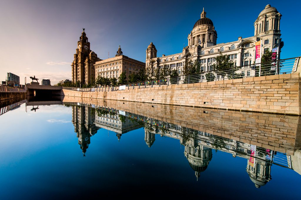 The Three Graces of Liverpool at Pier Head, with the blue sky reflecting off the water. 