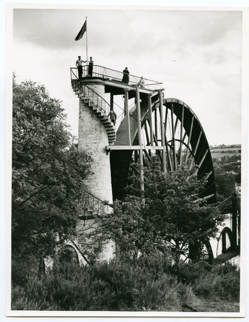 Black and white photo of The Great Laxey Wheel with four people at the top 
