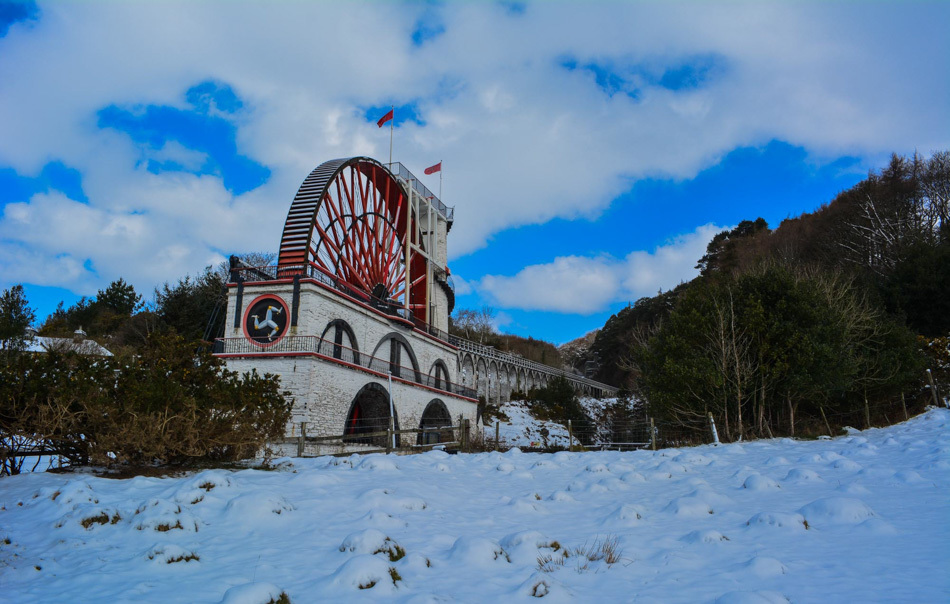 The red Laxey Wheel on a winters dayt with snow on the ground and a blue sky 