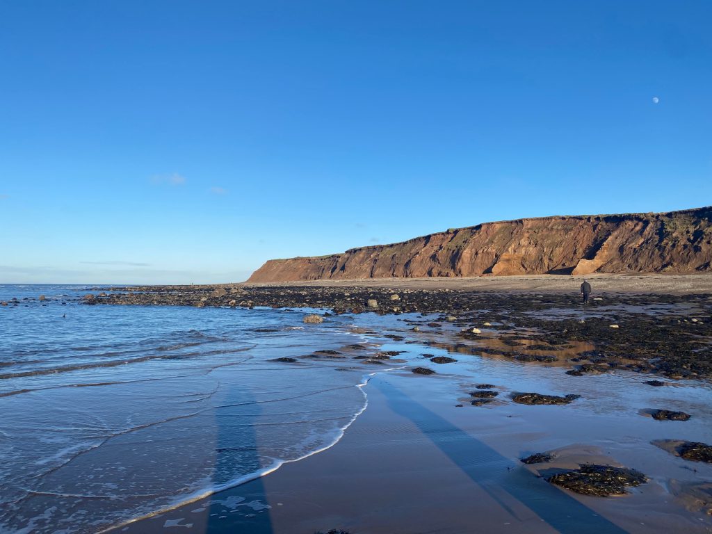 Blue winter skies with the sea washing up against the shoreline and cliffs in the background