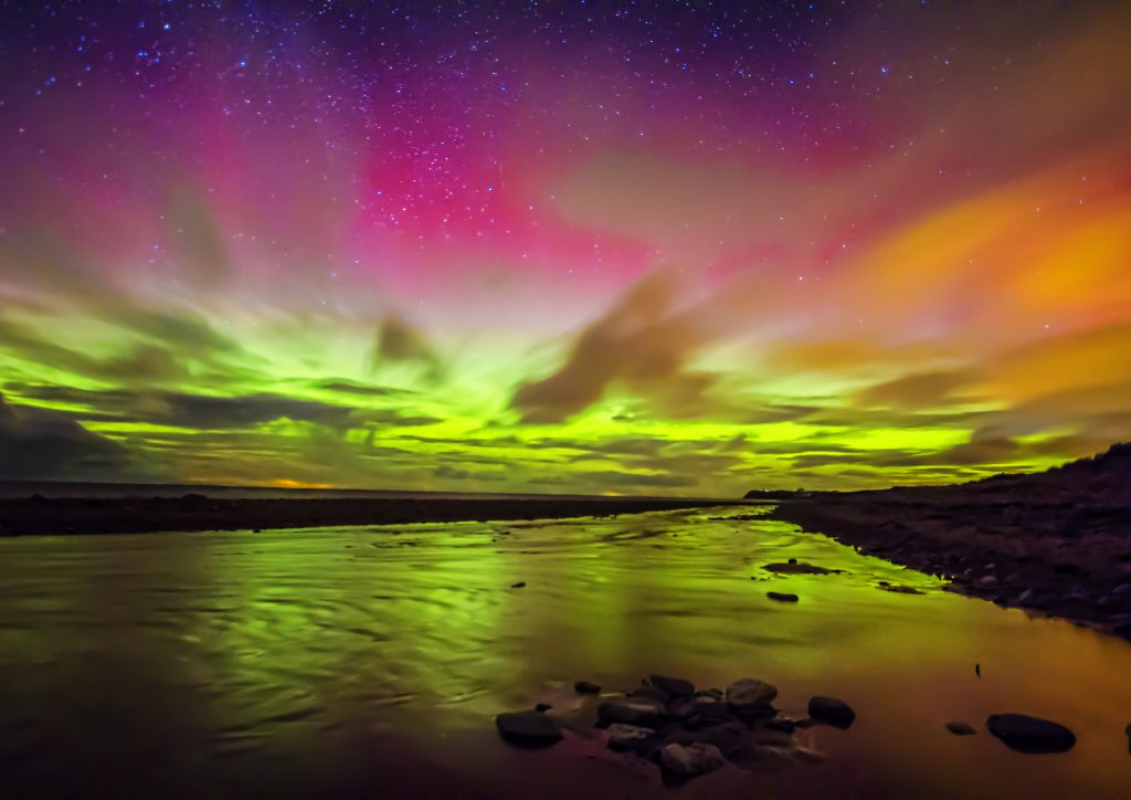 The colourful northern lights overlooking a beach in the Isle of Man 