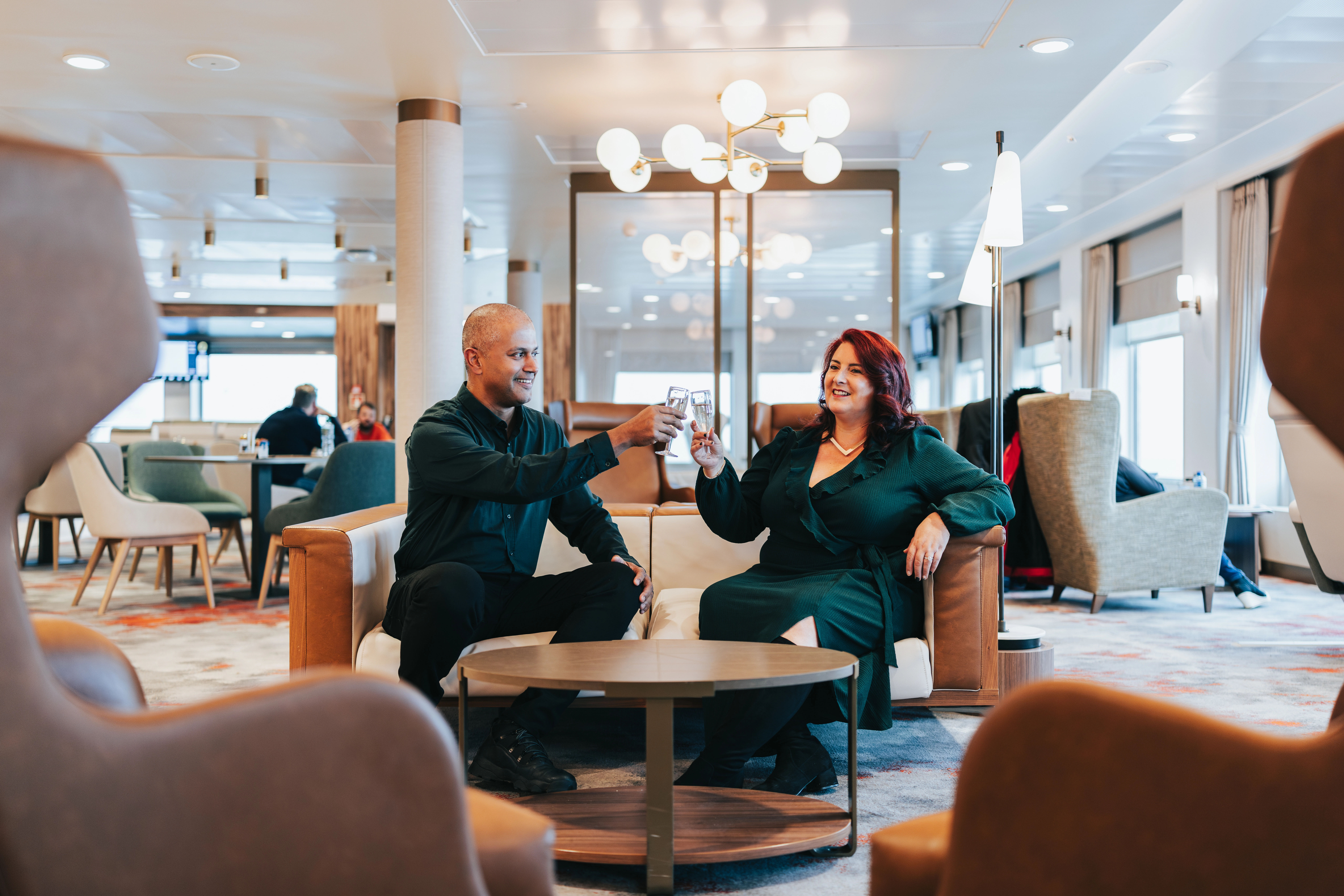 Two people sat in the Barrule lounge toasting two glasses of fizz