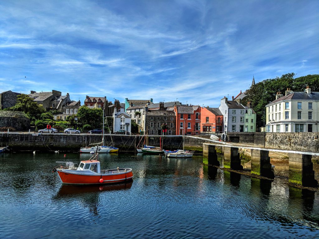 Boats sitting in Castletown Harbour on a sunny day with colourful houses in the background