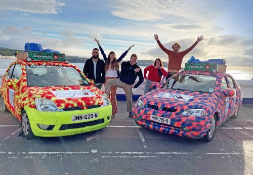 Two charity race cars, decorate with furry patterns at the harbour by the sea with five people celebrating