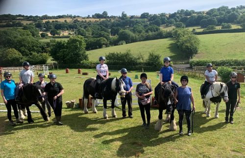 Children on horses with adult instructors in a field in the sun