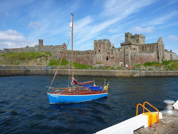 A little blue boat approaches Peel harbour with the imposing Peel Castle in the backdrop