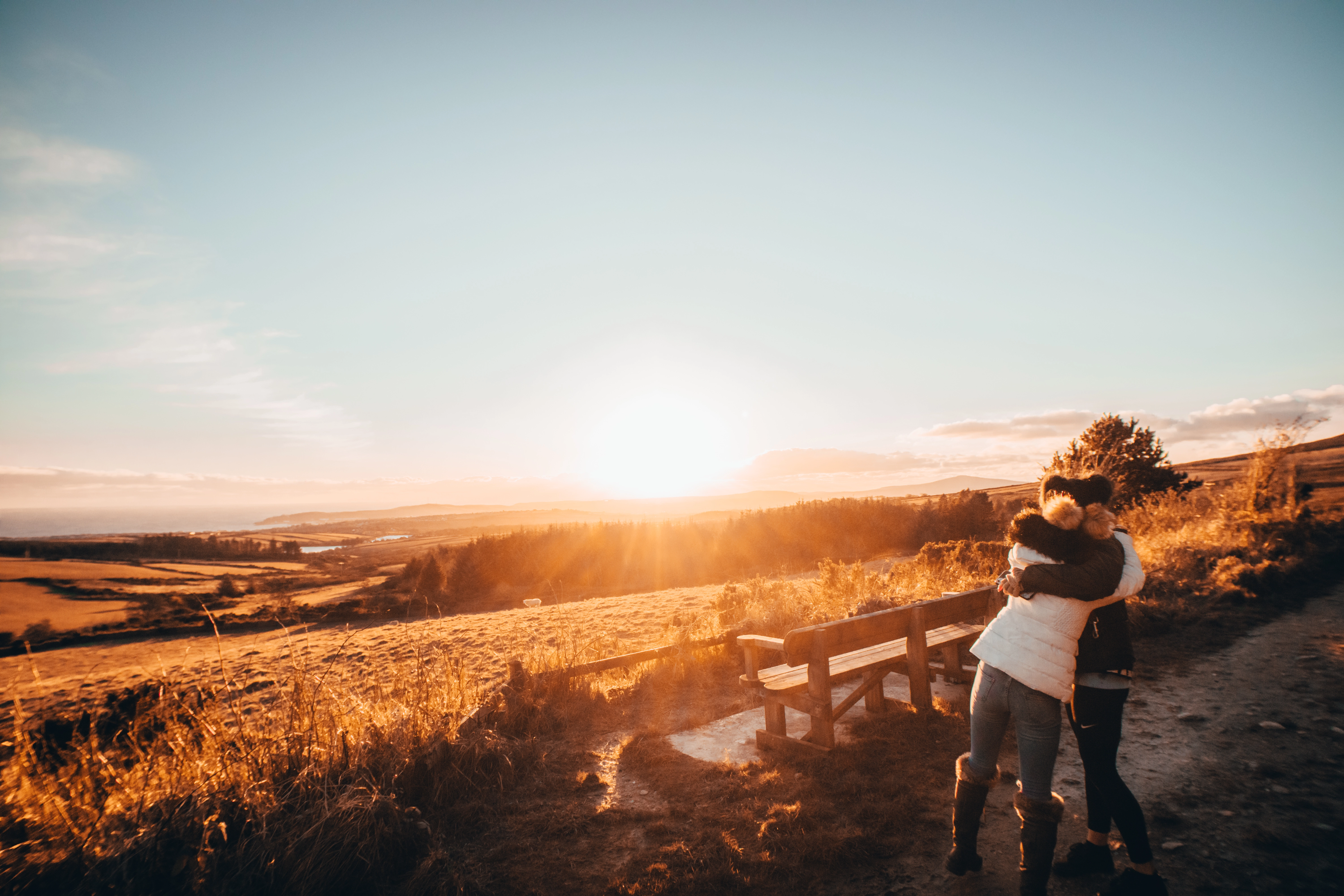 A sunset on a mountain with two people hugging 