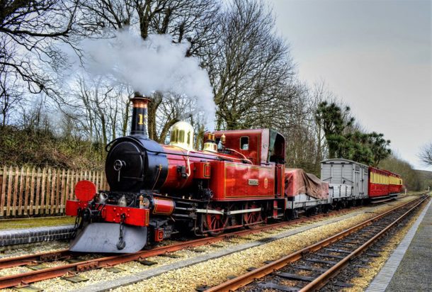 A red steam train with steam coming out - part of the Isle of Man Steam Railway