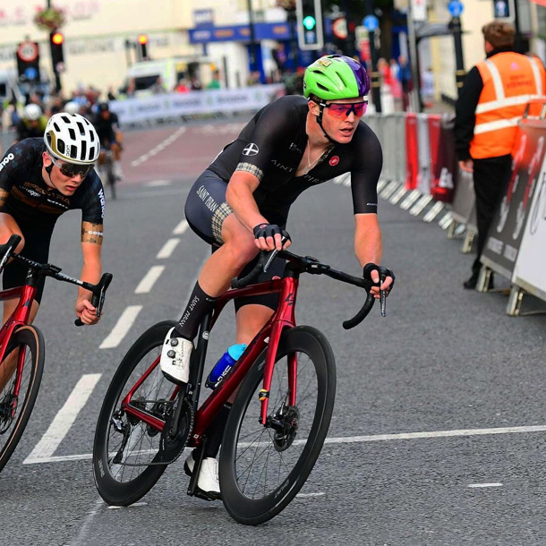 Tom Mazzone cycling with a green and purple helmet with another cyclist behind him
