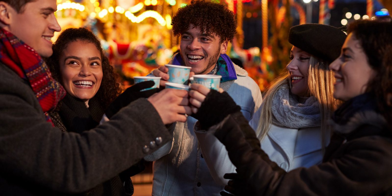Group of friends at a Christmas market enjoying a warm festive drink and having fun
